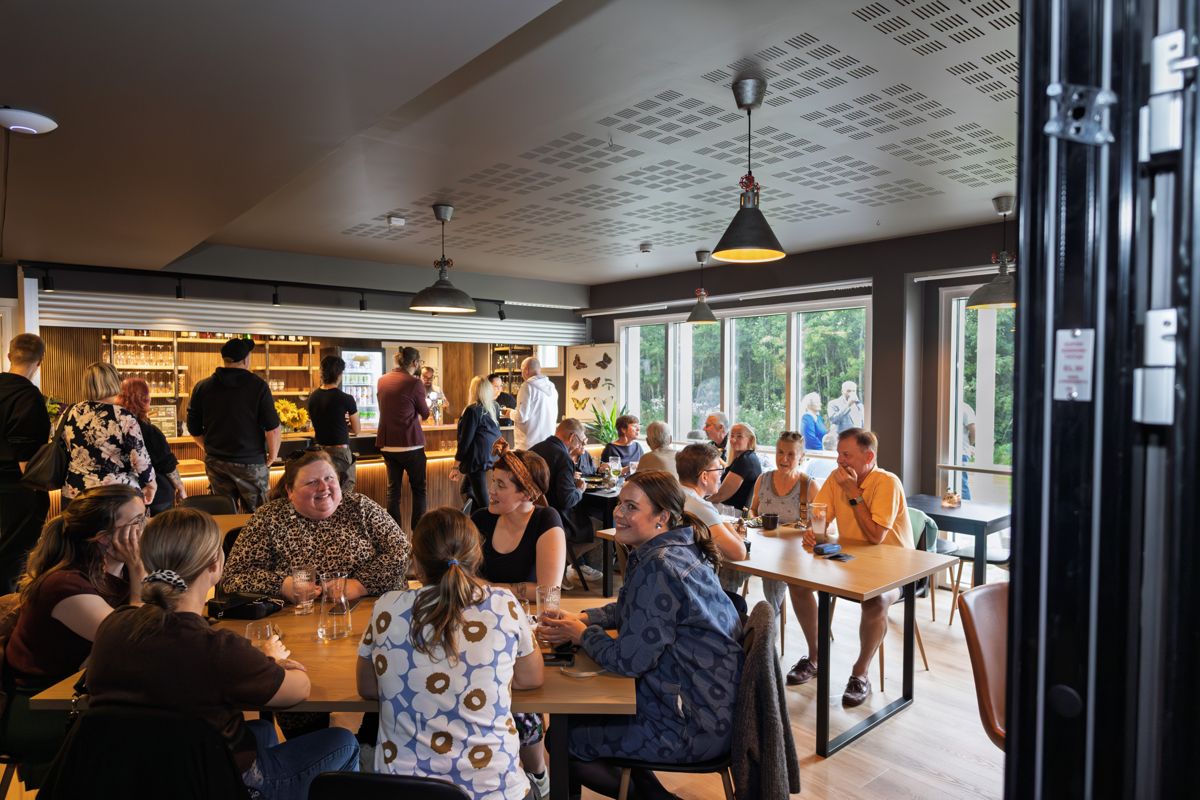 Ravintolasali täynnä asiakkaita, tammipöydät ja isot ikkunat