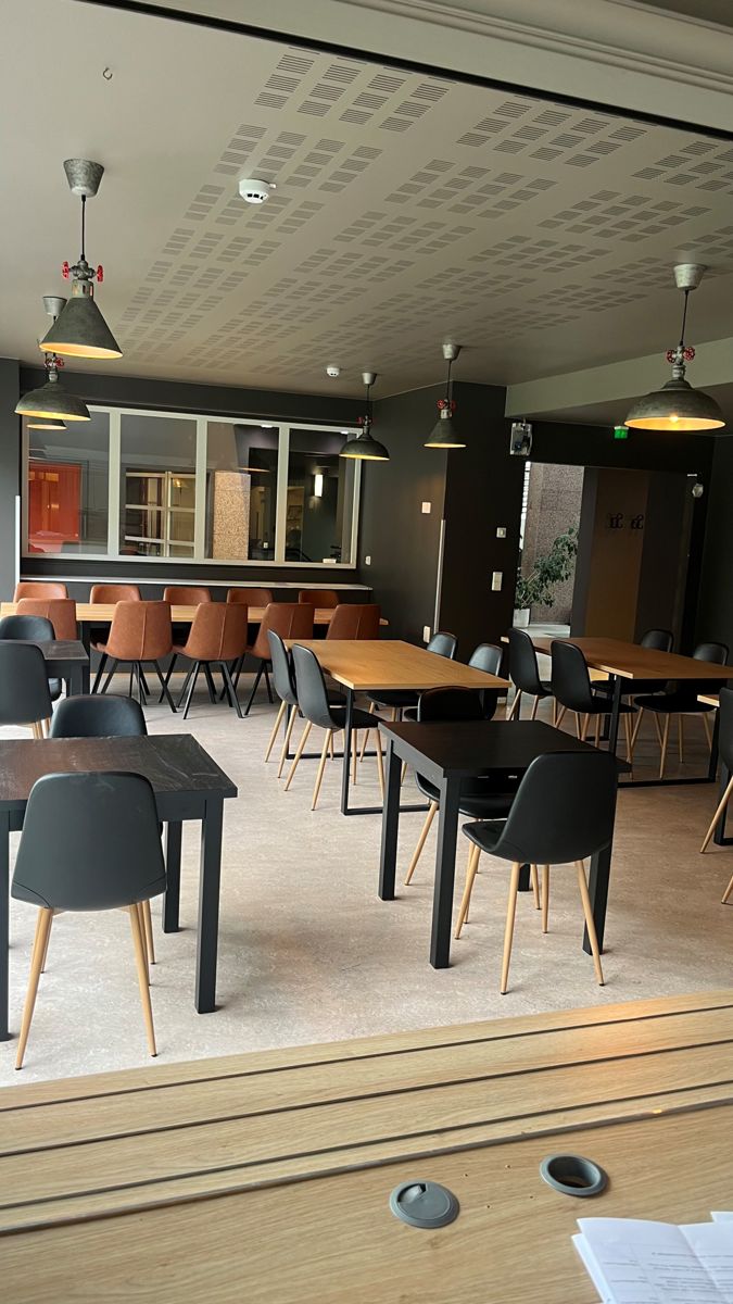 Tyhjä ravintolasali, tummat tuolit, tammipöydät ja mustat riippuvalaisimet
